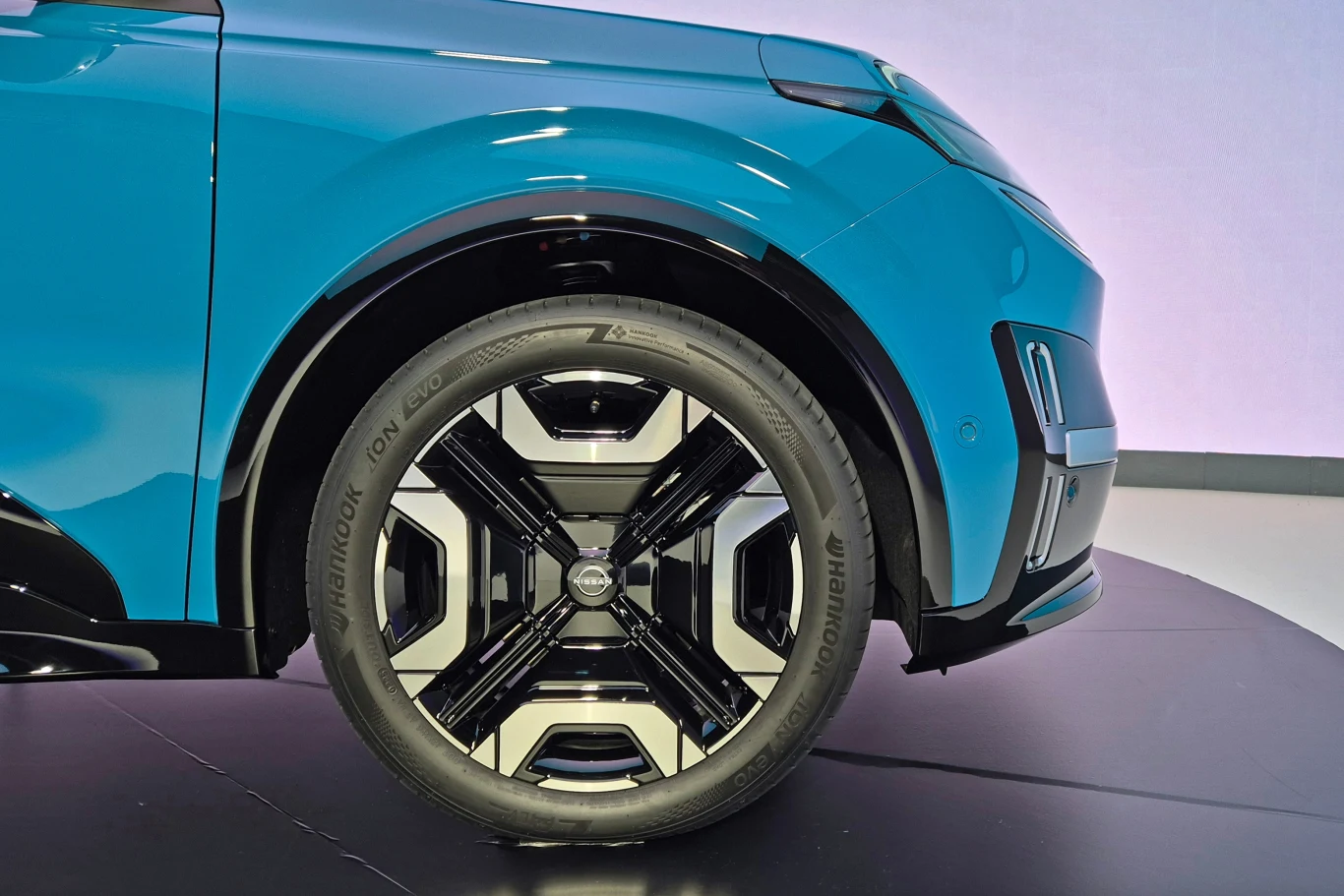 Fragment nowoczesnego niebieskiego auta zbliżenie na felgę i oponę o innowacyjnym wzorze na czarnym tle.