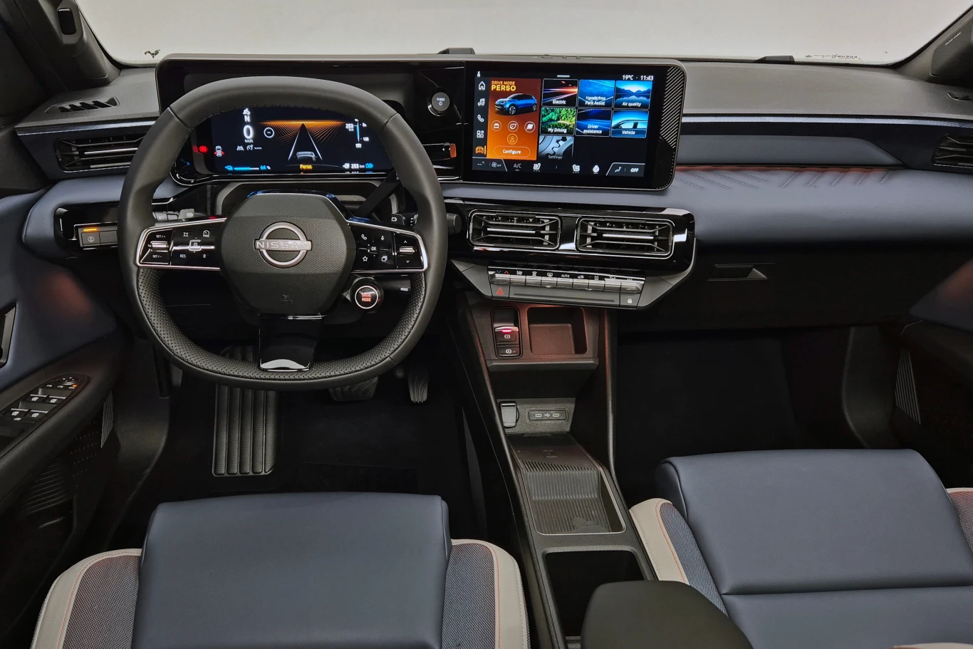 Wnętrze samochodu z eleganckim kokpitem, nowoczesnym panelem sterowania i dużymi ekranami dotykowymi. Kierownica znajduje się po lewej stronie, a siedzenia wydają się wyściełane ciemnym materiałem. Wszystko jest utrzymane w stonowanej kolorystyce, z du...