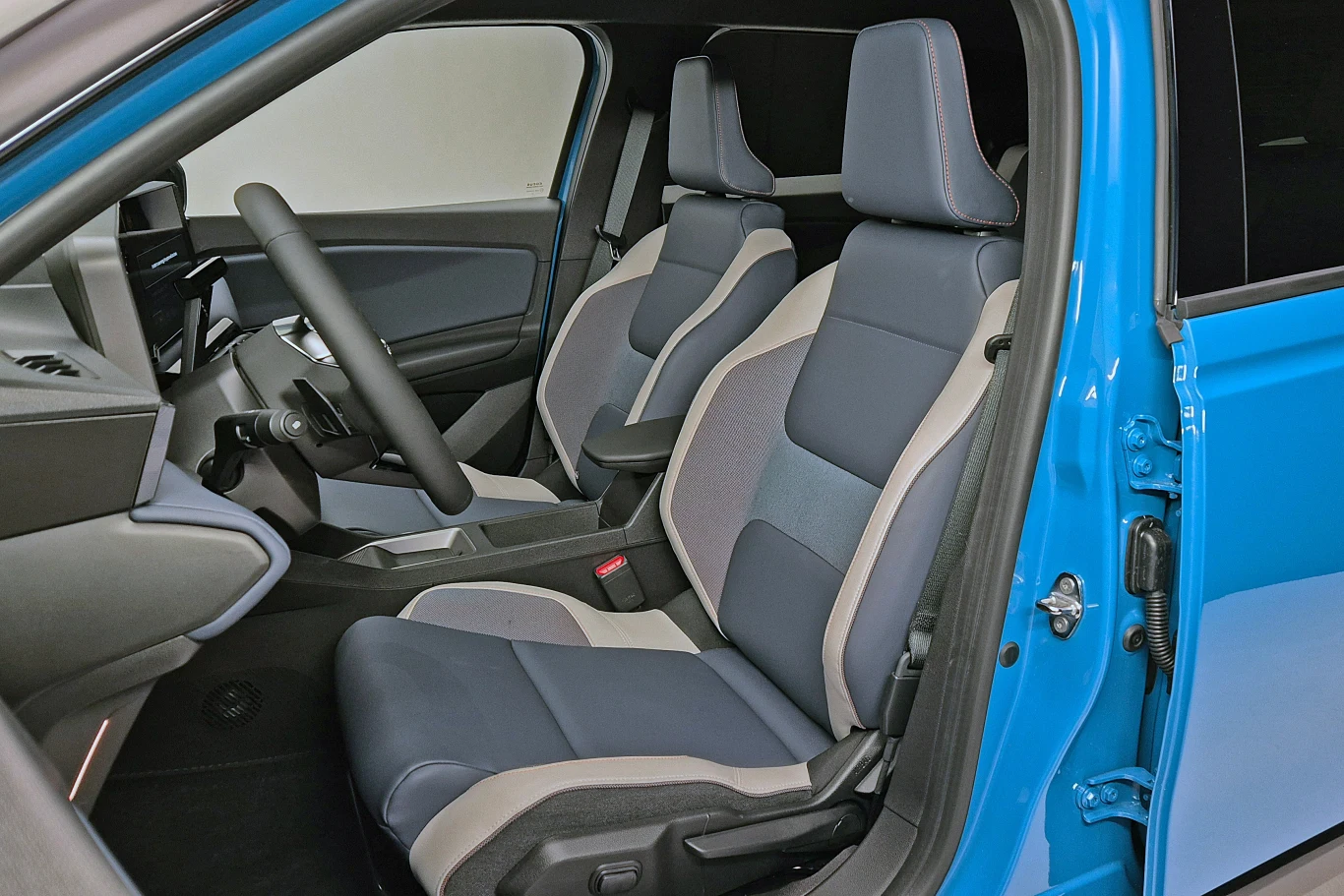 Wnętrze nowoczesnego samochodu w odcieniach niebieskiego i szarego. Centralnym punktem są ergonomiczne fotele z regulacją, obok widoczna jest kierownica i elementy deski rozdzielczej. Elegancki design zapewniający komfort podróży.