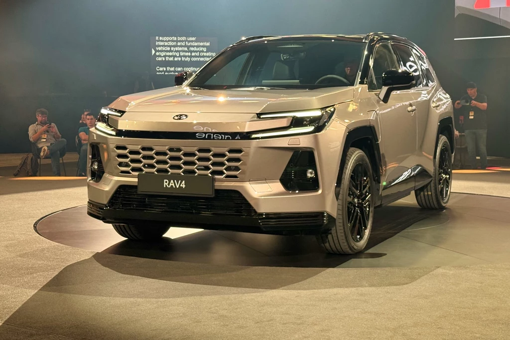 Choć powstała na tej samej platformie, nowa Toyota RAV4 wygląda zupełnie inaczej SUV RAV4 na podwyższonej platformie podczas prezentacji motoryzacyjnej, z widownią w tle.