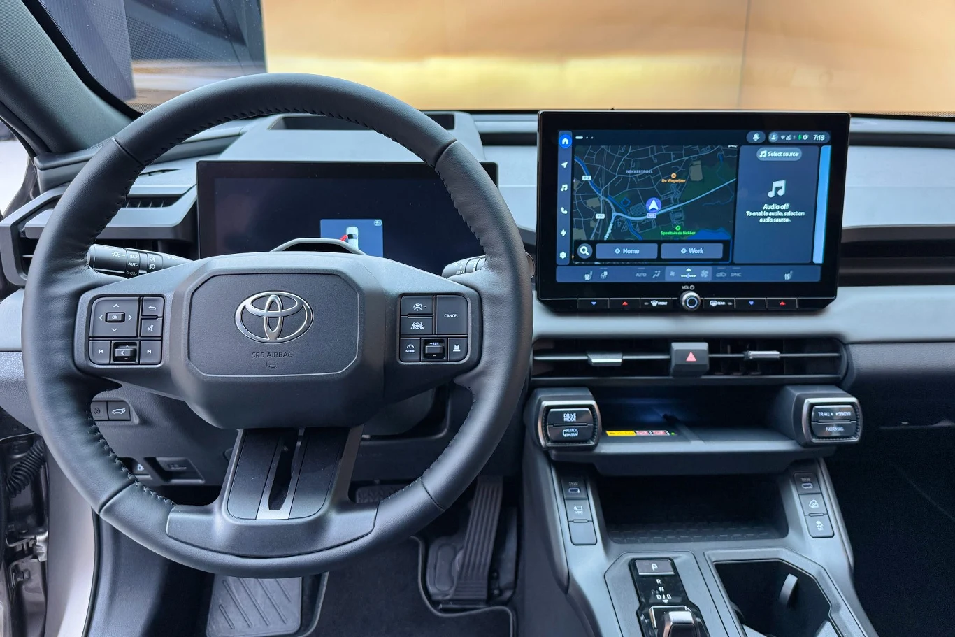 Wnętrze samochodu z widoczną kierownicą marki Toyota i nowoczesnym panelem sterującym z dużym ekranem dotykowym, pokazującym mapę oraz aplikację muzyczną. Wnętrze ma elegancki i funkcjonalny design.