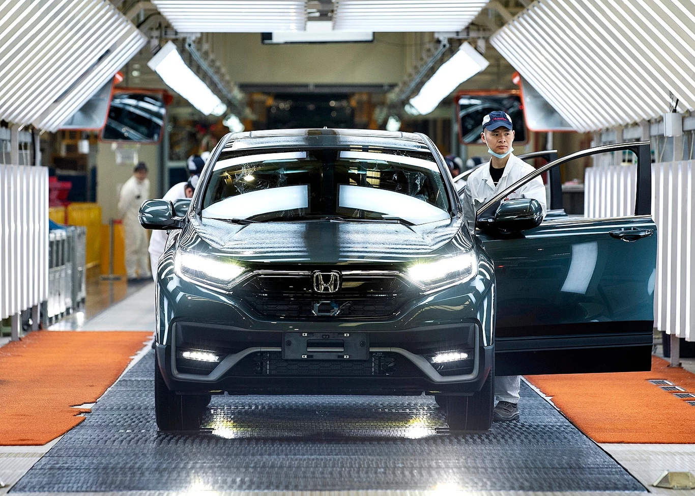 Honda robi krok w tył na drodze do elektromobilności. Stawia na samochody hybrydowe Nowoczesny samochód Honda SUV na linii produkcyjnej fabryki, wokół pojazdu pracownicy w białych uniformach kontrolujący jakość i stan samochodu, wyraźne oświetlenie miejsca pracy, otoczenie przemysłowe.