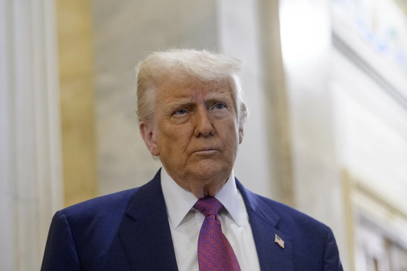 Setki tysięcy Ukraińców mogą zostać deportowane z USA. Plany administracji prezydenta Donalda Trumpa ujawnił "Washington Post" (zdjęcie ilustracyjne) Mężczyzna w średnim wieku w granatowym garniturze, białej koszuli i czerwonym krawacie, stojący w eleganckim, marmurowym wnętrzu; na klapie marynarki widoczna jest przypinka z flagą Stanów Zjednoczonych.