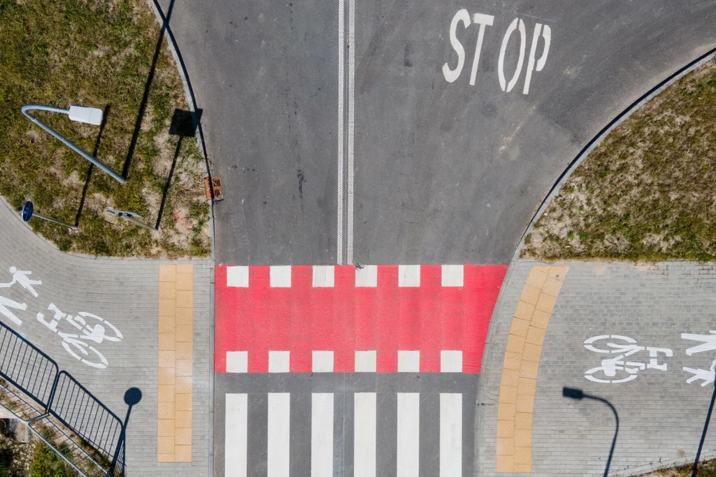 Czym są czerwone pasy dla rowerów? Pasy dla pieszych na skrzyżowaniu z czerwonym oznaczeniem, napisem STOP na jezdni oraz wydzielonymi ścieżkami rowerowymi po obu stronach.