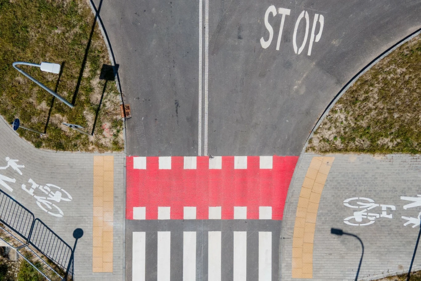 Pasy dla pieszych na skrzyżowaniu z czerwonym oznaczeniem, napisem STOP na jezdni oraz wydzielonymi ścieżkami rowerowymi po obu stronach.