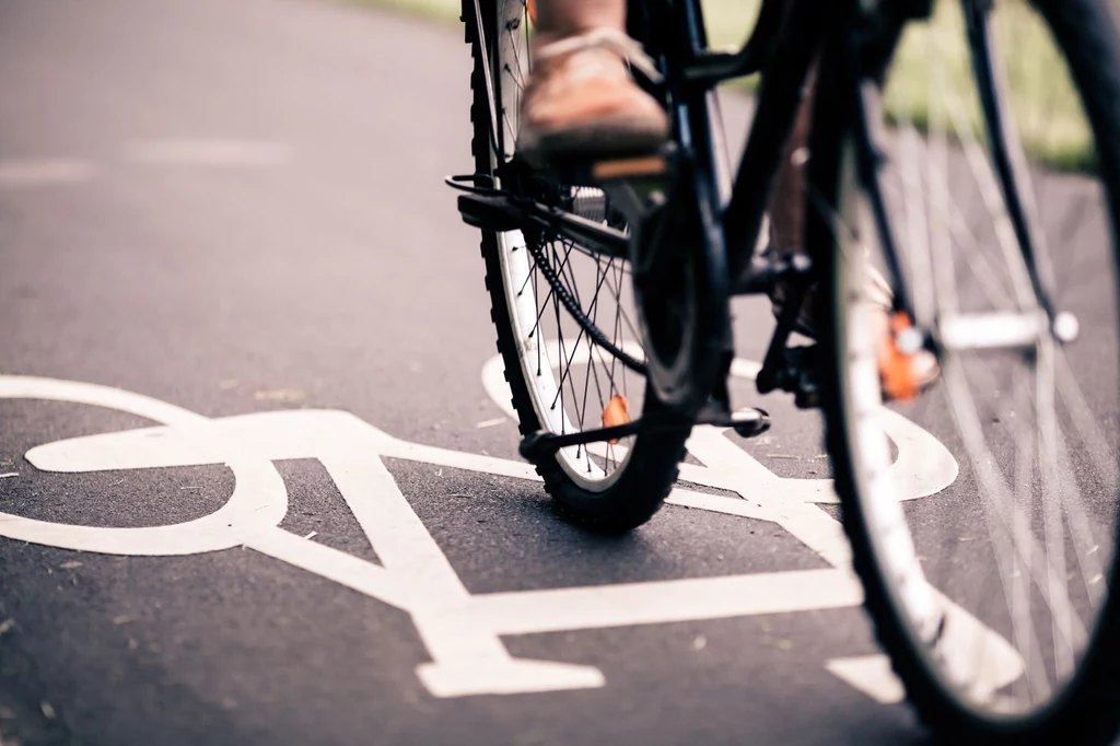 Czy rowerzysta ma pierwszeństwo na czerwonych pasach? Rower poruszający się po wyznaczonym pasie rowerowym z wyraźnym oznakowaniem na asfalcie, część rowerzysty oraz pedały widoczne w ruchu.