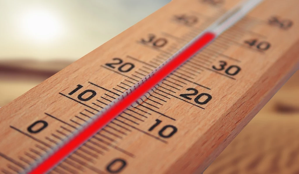 Fot. pixabay.com/ geralt Drewniany termometr rtęciowy pokazujący temperaturę powyżej 20 stopni Celsjusza, rozmyte tło sugerujące upał lub pustynne otoczenie.