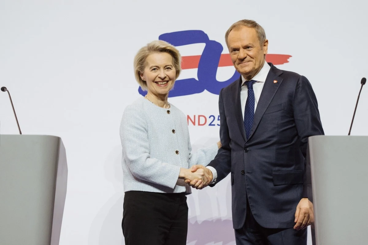 Francuskie media: Ursula von der Leyen spieszy z pomocą Donaldowi Tuskowi Kobieta i mężczyzna w eleganckich ubraniach podają sobie ręce na tle białej ściany z kolorowym logotypem oraz mównicami po obu stronach. Oboje uśmiechnięci, w oficjalnej atmosferze spotkania lub konferencji.