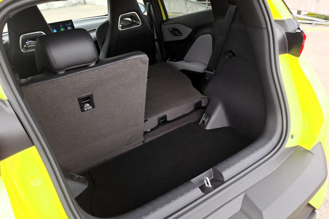 Bagażnik samochodu z rozłożoną częścią tylnej kanapy, żółte nadwozie widoczne przy krawędzi, tapicerka w odcieniach czerni i szarości oraz fragment wnętrza z przednimi fotelami.