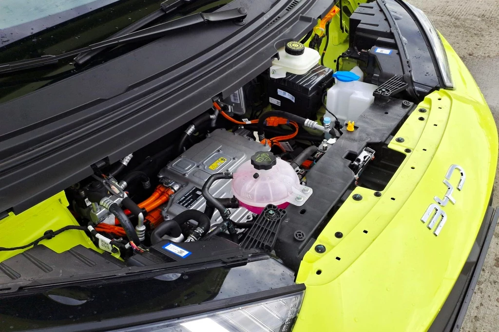 BYD Dolphin Surf dostępny jest w dwóch wariantach mocy - 88 KM i 156 KM. Silnik elektrycznego samochodu w jasnozielonej obudowie, widoczne przewody, zbiorniki płynów eksploatacyjnych oraz charakterystyczna instalacja wysokiego napięcia.