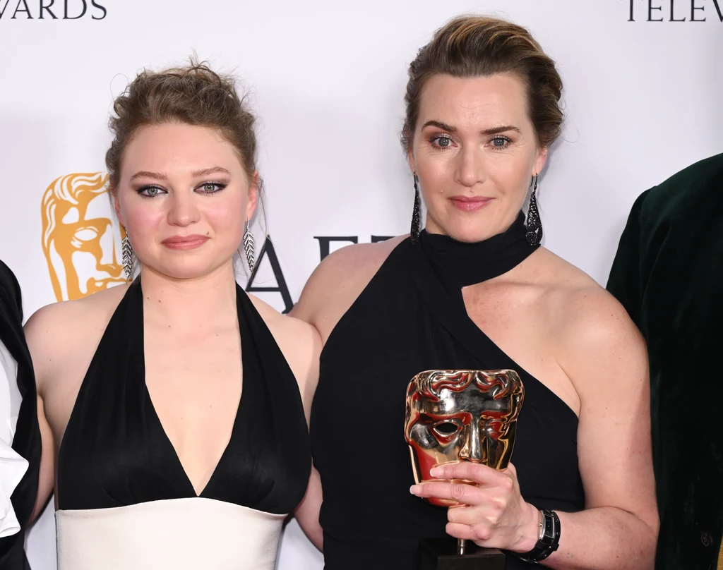 Kate Winslet jest dumna z córki Dwie kobiety w eleganckich, wieczorowych sukienkach stoją razem na tle ścianki z logo nagrody BAFTA, jedna z nich trzyma w dłoni statuetkę BAFTA i uśmiecha się lekko do aparatu.