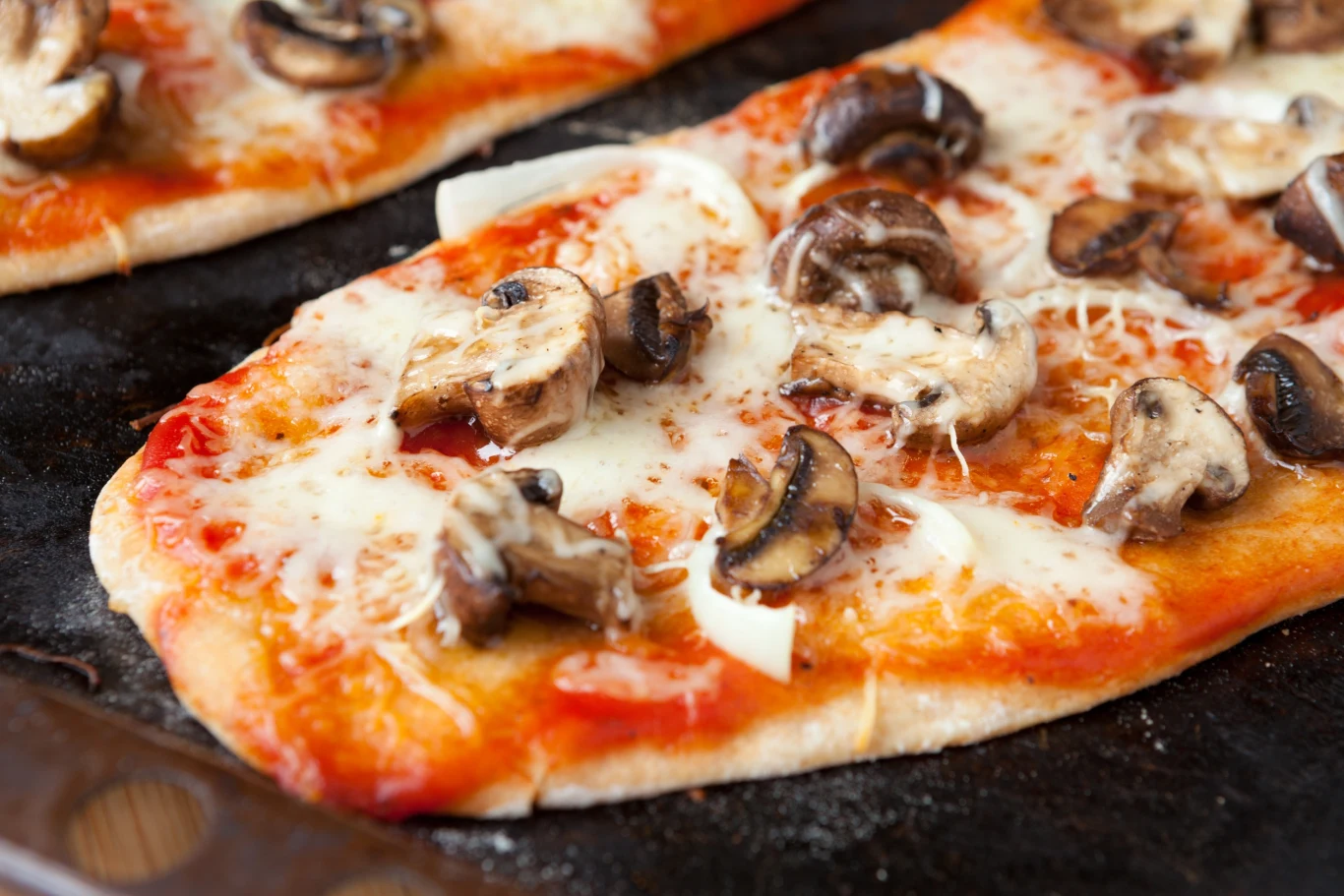 Prostokątna pizza z sosem pomidorowym, serem, plasterkami świeżych pieczarek i cebuli, upieczona na ciemnej blasze.