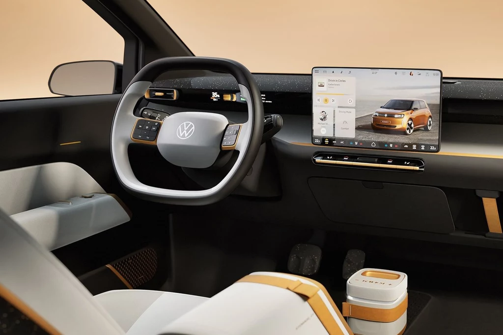Volkswagen ID. Every1 Nowoczesne wnętrze samochodu Volkswagen z cyfrowym wyświetlaczem na kierownicy i dużym ekranem dotykowym na konsoli centralnej; stylowe, minimalistyczne elementy wykończenia w bieli i pomarańczu.