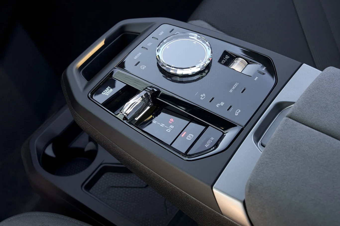 Panel sterowania w samochodzie z dużym chromowanym pokrętłem, przyciskami do sterowania multimediami i funkcjami pojazdu, znajdujący się na środkowym tunelu między fotelami.