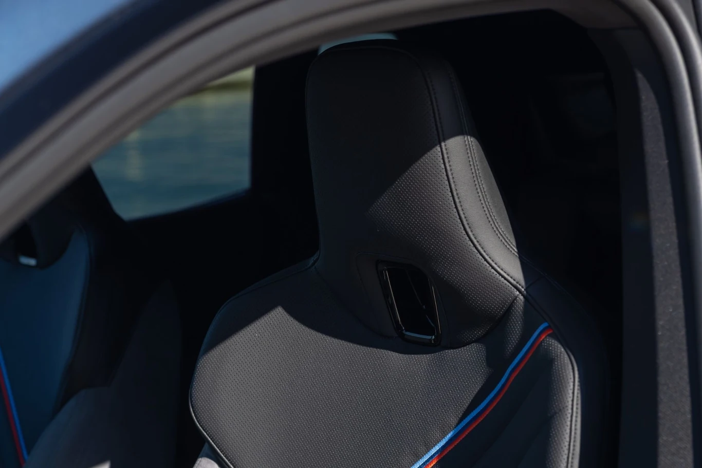 Czarny sportowy fotel samochodowy z ozdobnymi przeszyciami w kolorze niebieskim i czerwonym, widoczny przez otwarte drzwi pojazdu.