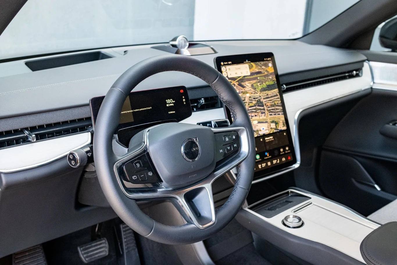 Nowoczesne wnętrze samochodu z dużym ekranem dotykowym centralnej konsoli, cyfrowymi wskaźnikami oraz minimalistycznym designem kokpitu; widoczna kierownica i szczegóły panelu przedniego.