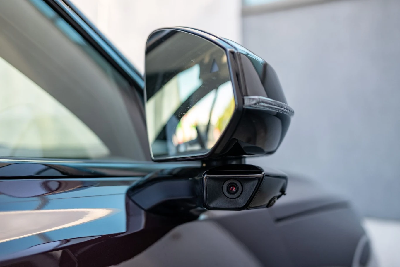 elektrycznie sterowane lusterko boczne samochodu wyposażone w dodatkową kamerę wspomagającą obserwację otoczenia pojazdu, zamontowane na błyszczącej karoserii w kolorze czarnym