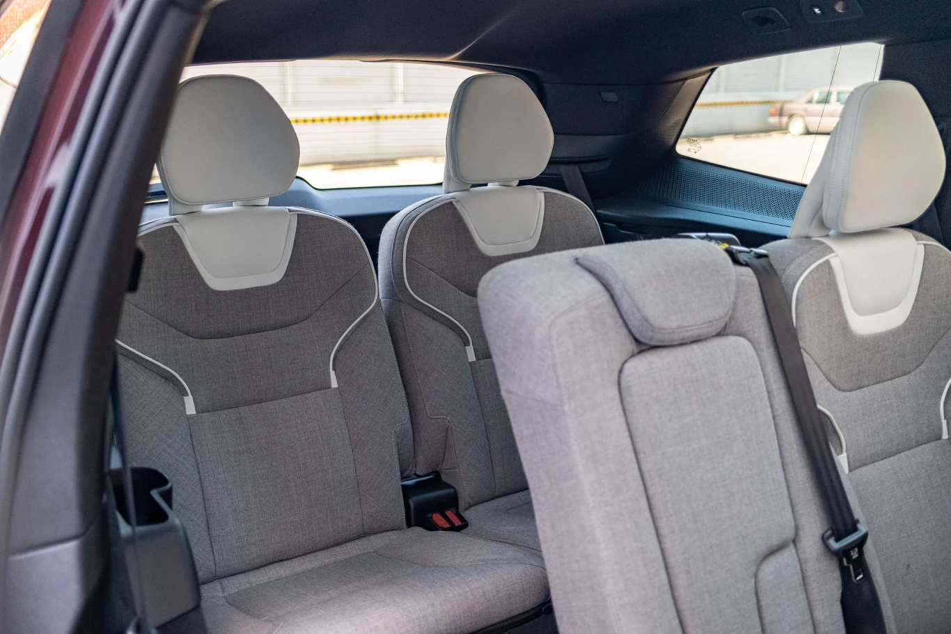 Wnętrze samochodu z jasnoszarymi fotelami, widoczny drugi i trzeci rząd siedzeń, tapicerka wykonana z materiału, przestronne miejsce pasażerskie.