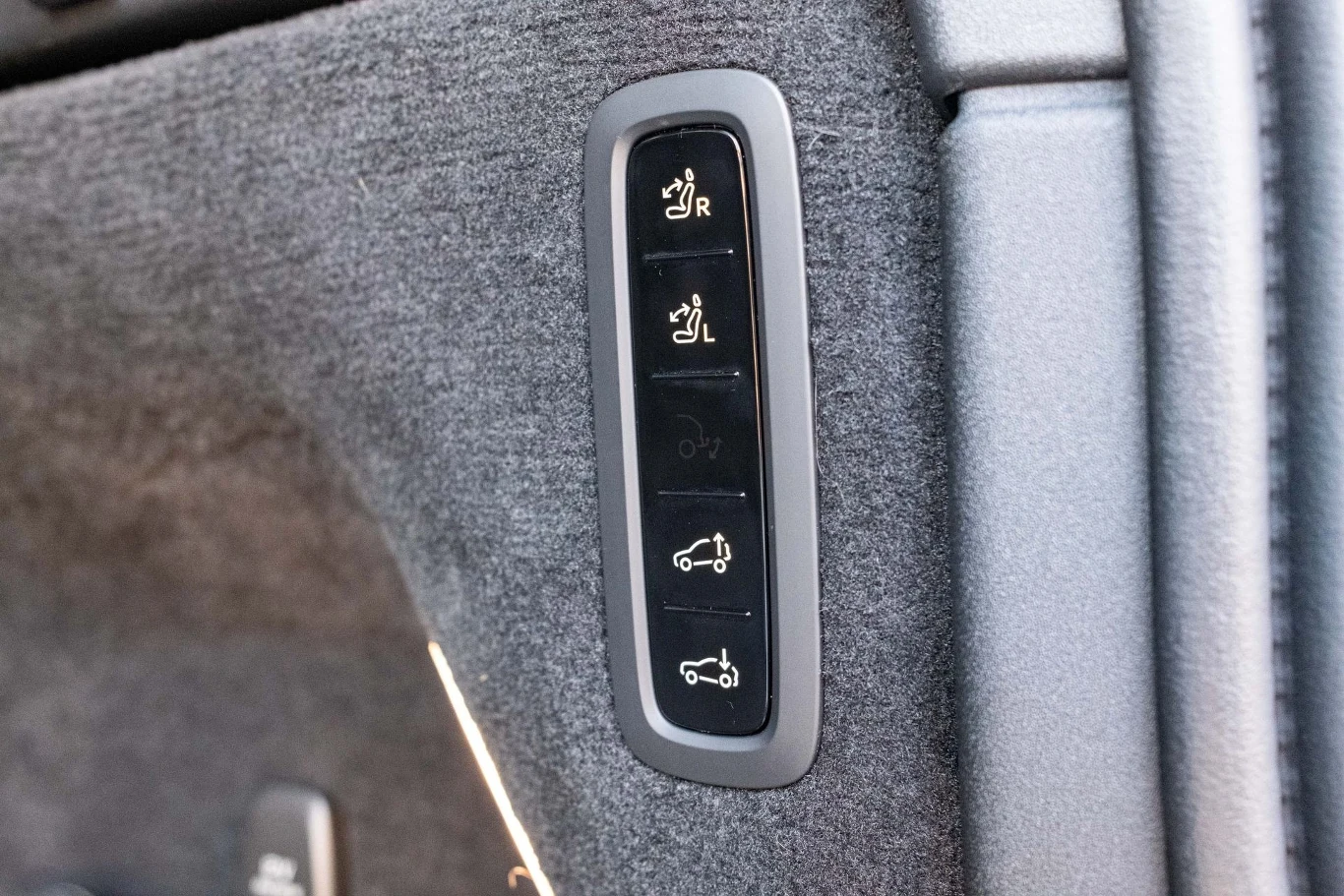Panel przycisków w samochodzie umieszczony na tapicerce, zawierający cztery przyciski służące do obsługi funkcji bagażnika i tylnych siedzeń.