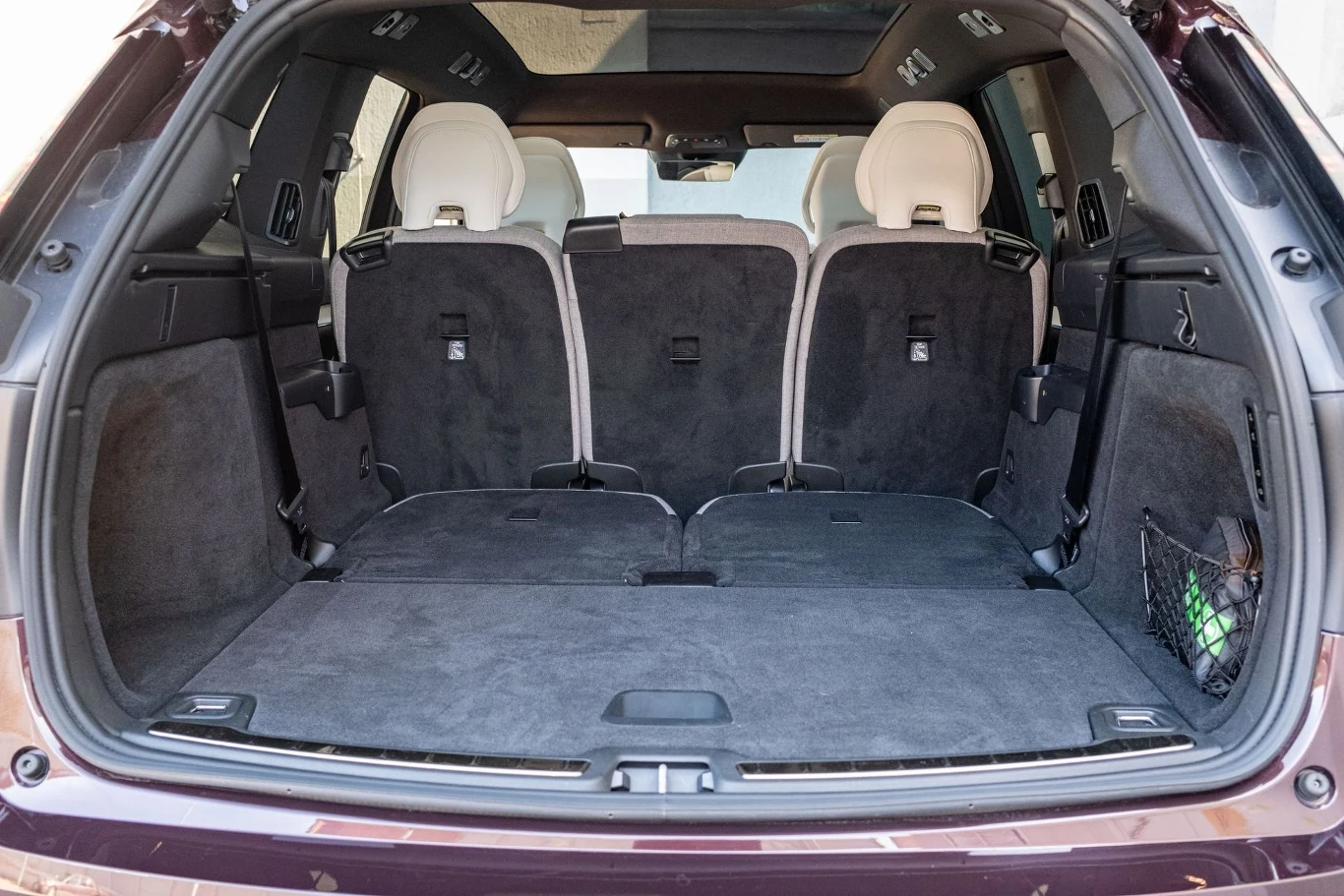 Przestronna przestrzeń bagażowa SUV-a z rozłożonymi siedzeniami trzeciego rzędu, tapicerka w ciemnych kolorach, dookoła elementy wyposażenia samochodu, po bokach kieszonki i gniazdka.