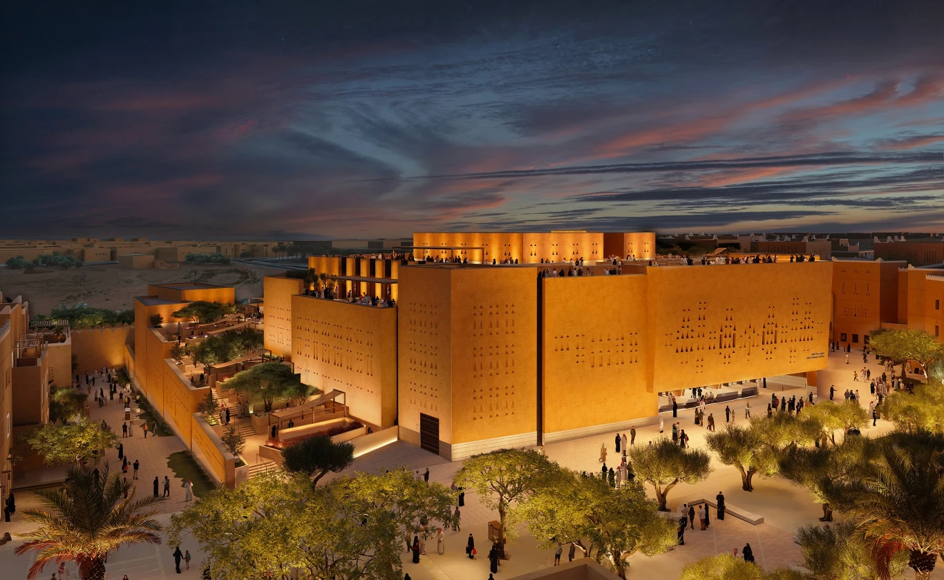 Projekt muzeum Asaan autorstwa Zahy Hadid Architects Nowoczesny kompleks budynków o ciepłych piaskowych barwach w otoczeniu bujnej zieleni i palm, iluminowany światłami o zmierzchu, z tłumem ludzi spacerujących po szerokich alejkach.