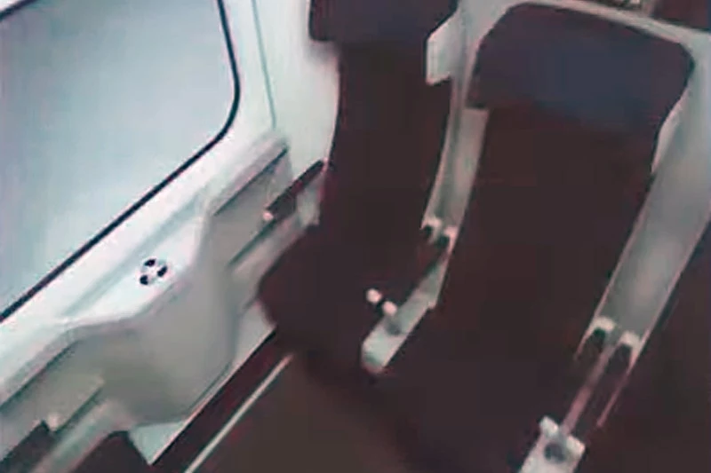 Wnętrze nowego wagonu 2. klasy dla pociągów PKP Intercity. Dwa puste siedzenia w nowoczesnym wagonie pociągu, przy oknie i stoliku, utrzymane w ciemnych kolorach, z jasnym tłem ściany.