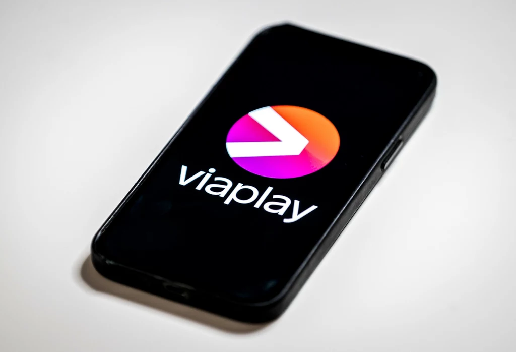 Gdzie trafią treści filmowe i sportowe z Viaplay? Smartfon leżący na białym tle, na ekranie wyświetlone kolorowe logo Viaplay na czarnym tle