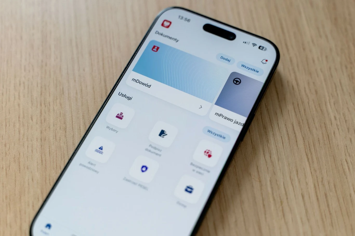 Ekran smartfona z otwartą aplikacją umożliwiającą dostęp do dokumentów i usług cyfrowych, wyświetlany na jasnym drewnianym blacie.