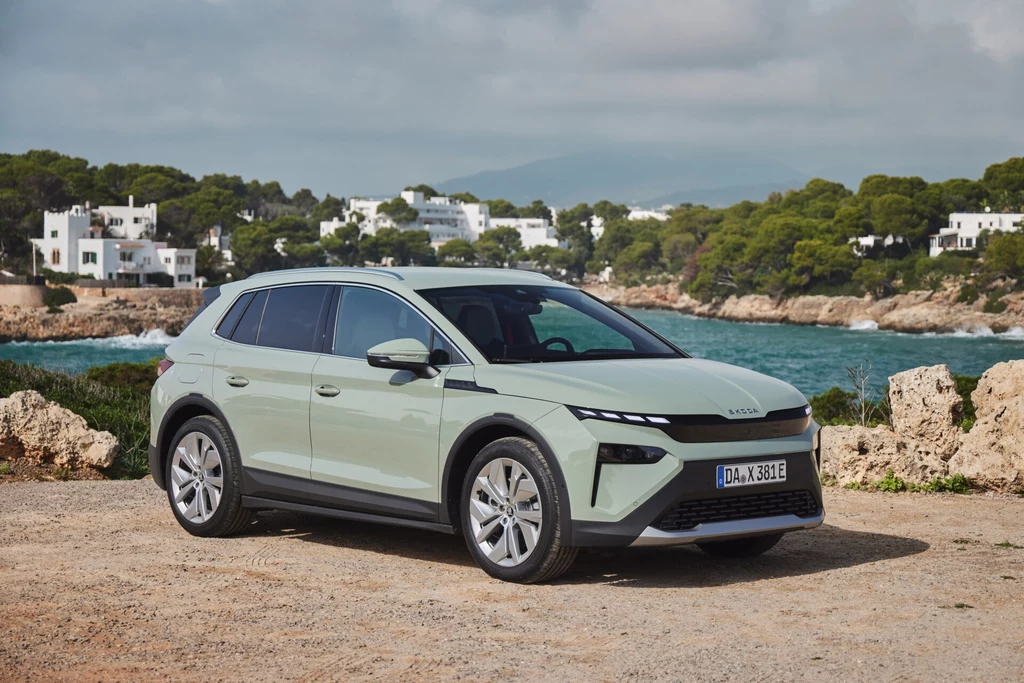 W kwietniu na Starym Kontynencie sprzedano 8 070 egzemplarzy Skody Elroq. Jasnozielony samochód elektryczny SUV stoi na tle wybrzeża z morzem, wokół roślinność śródziemnomorska i białe domy, w oddali zalesione wzgórza.