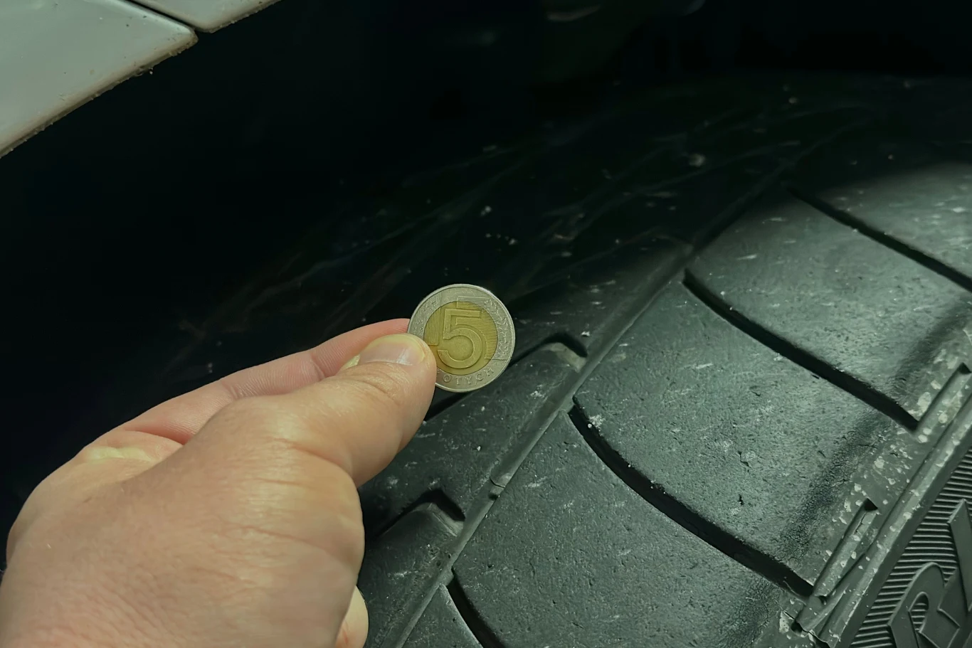 Moneta o nominale pięciu złotych przykładana do bieżnika opony samochodowej w celu pokazania głębokości rowków i stopnia zużycia opony.