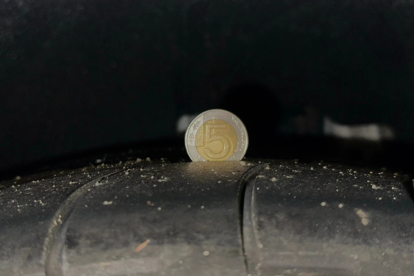 Pięciozłotowa moneta umieszczona w rowku opony samochodowej, pokazująca stopień zużycia bieżnika.
