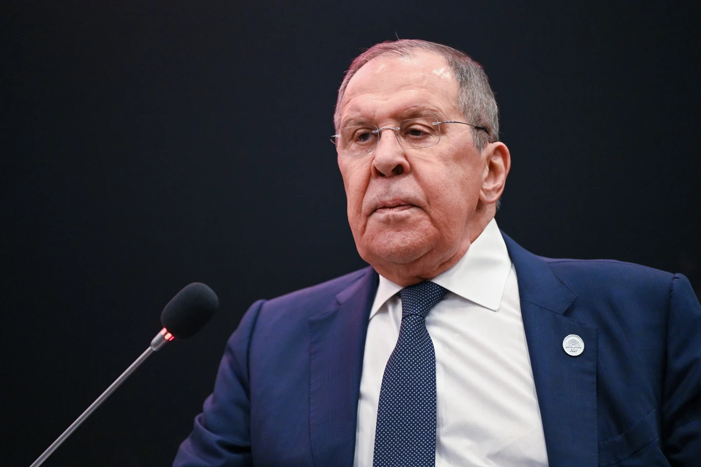 Siergiej Ławrow: Rosja będzie gotowa przekazać Ukrainie dokument z warunkami pokoju po wymianie więźniów Mężczyzna w garniturze i krawacie stoi przy mikrofonie na ciemnym tle, ma poważny wyraz twarzy, widoczna jest odznaka na klapie marynarki.