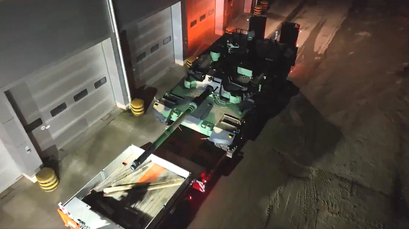 Polska armia rozmieszcza potężną broń na granicy z Rosją Czołg przewożony na lawetowej naczepie w nocy, oświetlenie generuje kontrastowe cienie, obok widoczne przemysłowe budynki oraz asfaltowa powierzchnia placu.