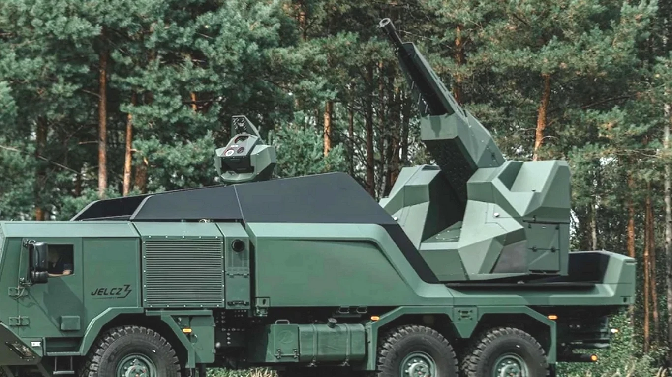 Oto potężne wsparcie dla polskiej tarczy przeciwlotniczej Opancerzony pojazd wojskowy z zamontowanym systemem artylerii przeciwlotniczej, pomalowany w matowy zielony kamuflaż, stoi na tle gęstego lasu sosnowego.