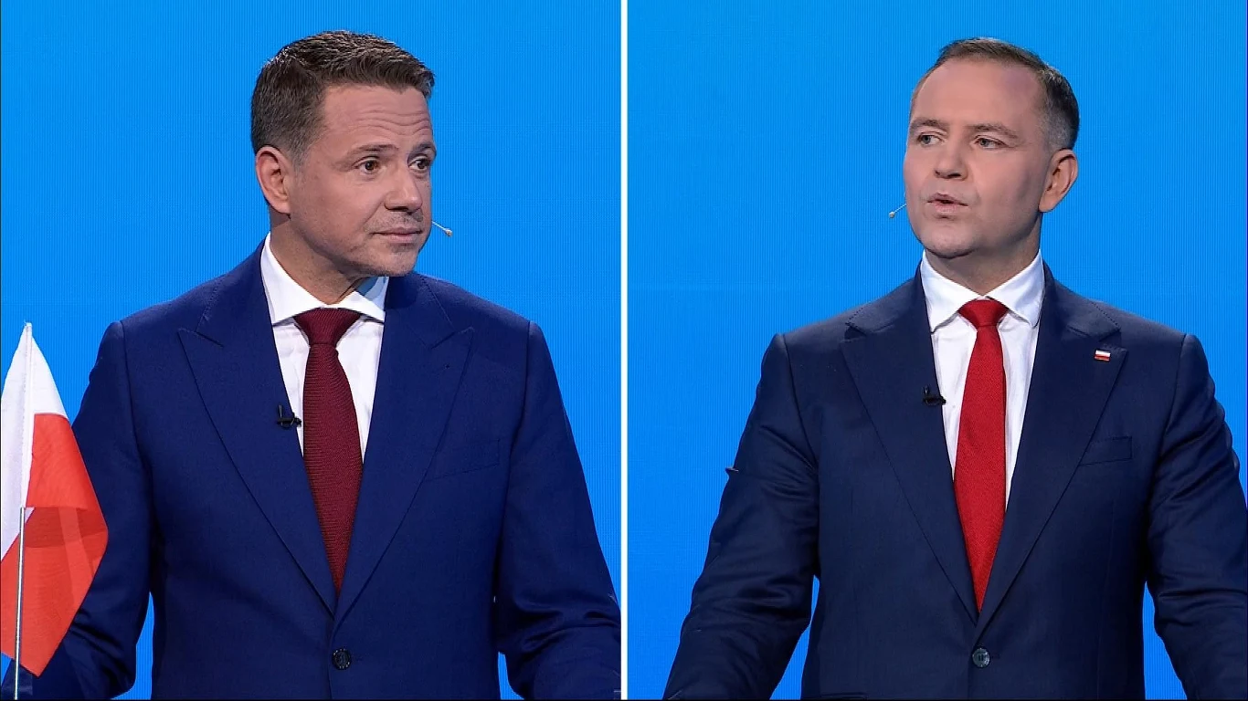 W debacie prezydenckiej pojawił się temat mieszkań komunalnych Dwóch mężczyzn ubranych w ciemne garnitury z czerwonymi krawatami stoi na tle jasnoniebieskiego ekranu, każdy z nich korzysta z mikrofonu nagłownego, po lewej widoczna biało-czerwona flaga.