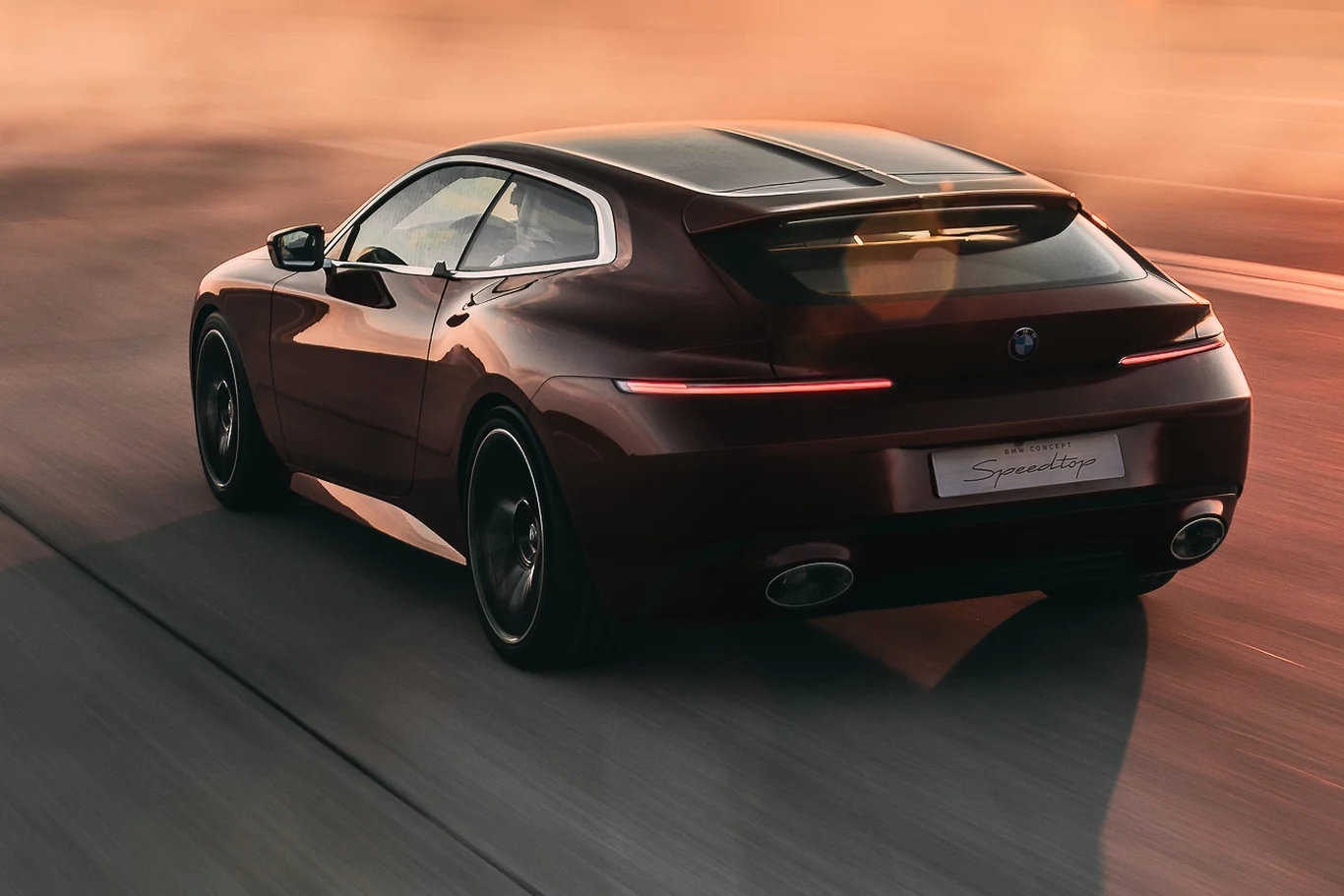 Luksusowy, sportowy samochód w bordowym kolorze jedzie po drodze o zachodzie słońca, światło lamp tylnych delikatnie podkreśla elegancką sylwetkę pojazdu.