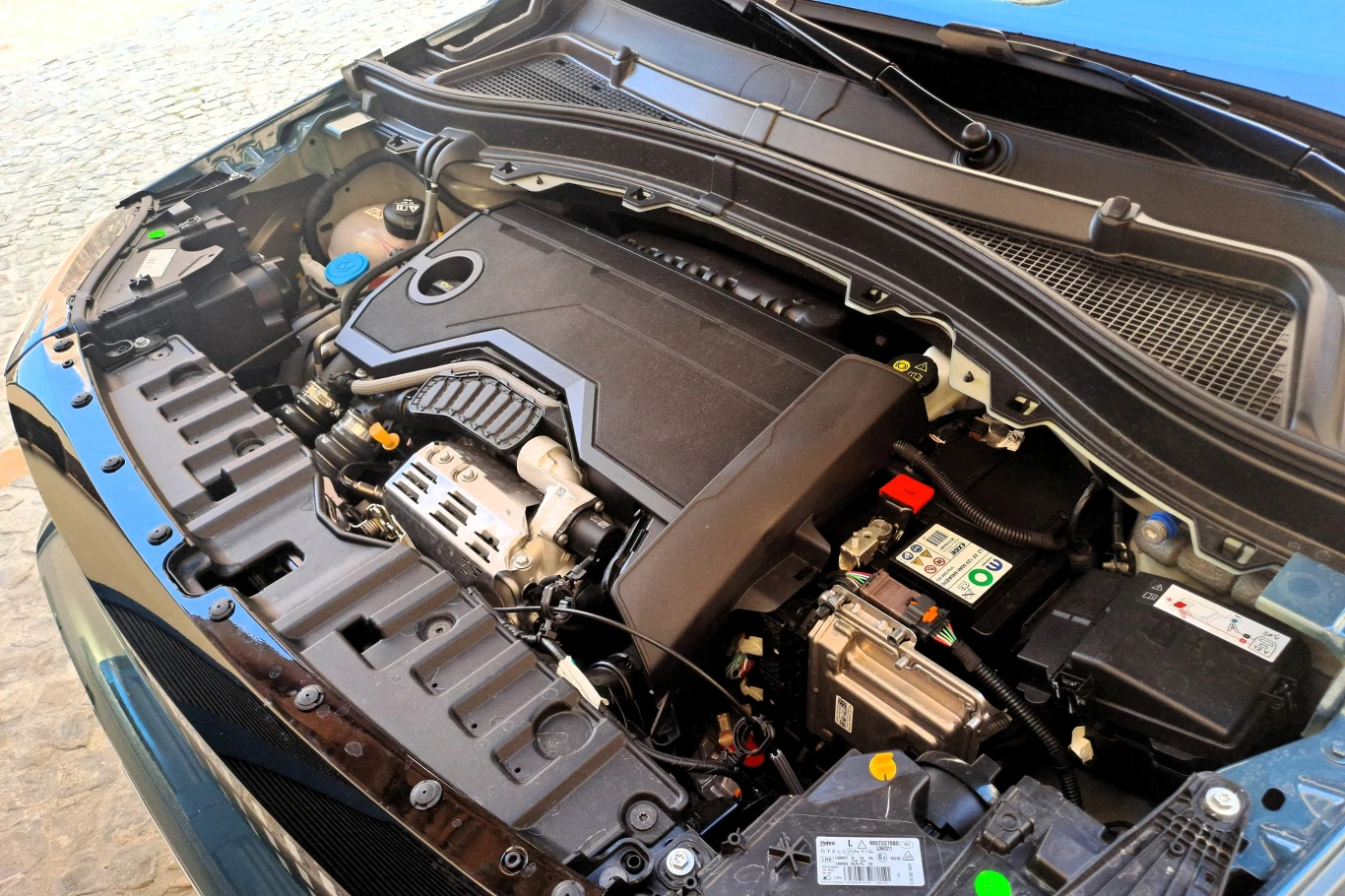 Za wprawianie w ruch hybrydowej Grande Pandy odpowiada 100-konny benzynowy silnik 1.2 wspierany przez 28,5-konną instalację elektryczną. Komora silnika samochodu osobowego z widocznym silnikiem, akumulatorem i innymi elementami układu mechanicznego. Wszystkie komponenty są czyste i dobrze utrzymane, sugerując niedawny przegląd lub nowy pojazd.