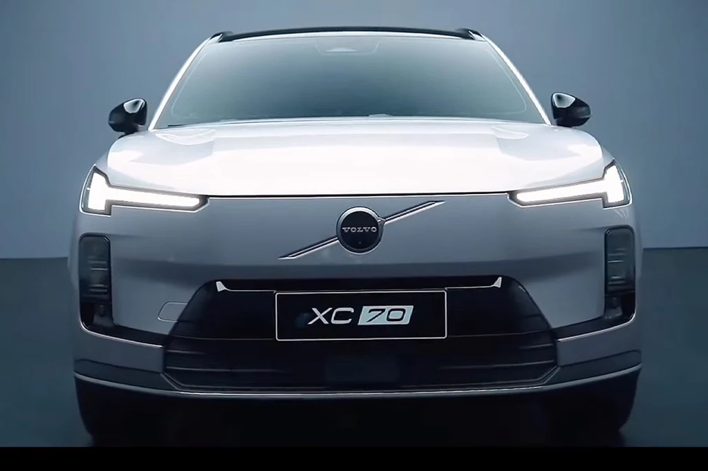 Stylizacja nadwozia XC70 nawiązuje do elektrycznych modeli marki Przód nowoczesnego, srebrnego samochodu Volvo XC70 z charakterystycznym logo marki i światłami LED, uchwycony na tle jednolitej, niebieskoszarej ściany.