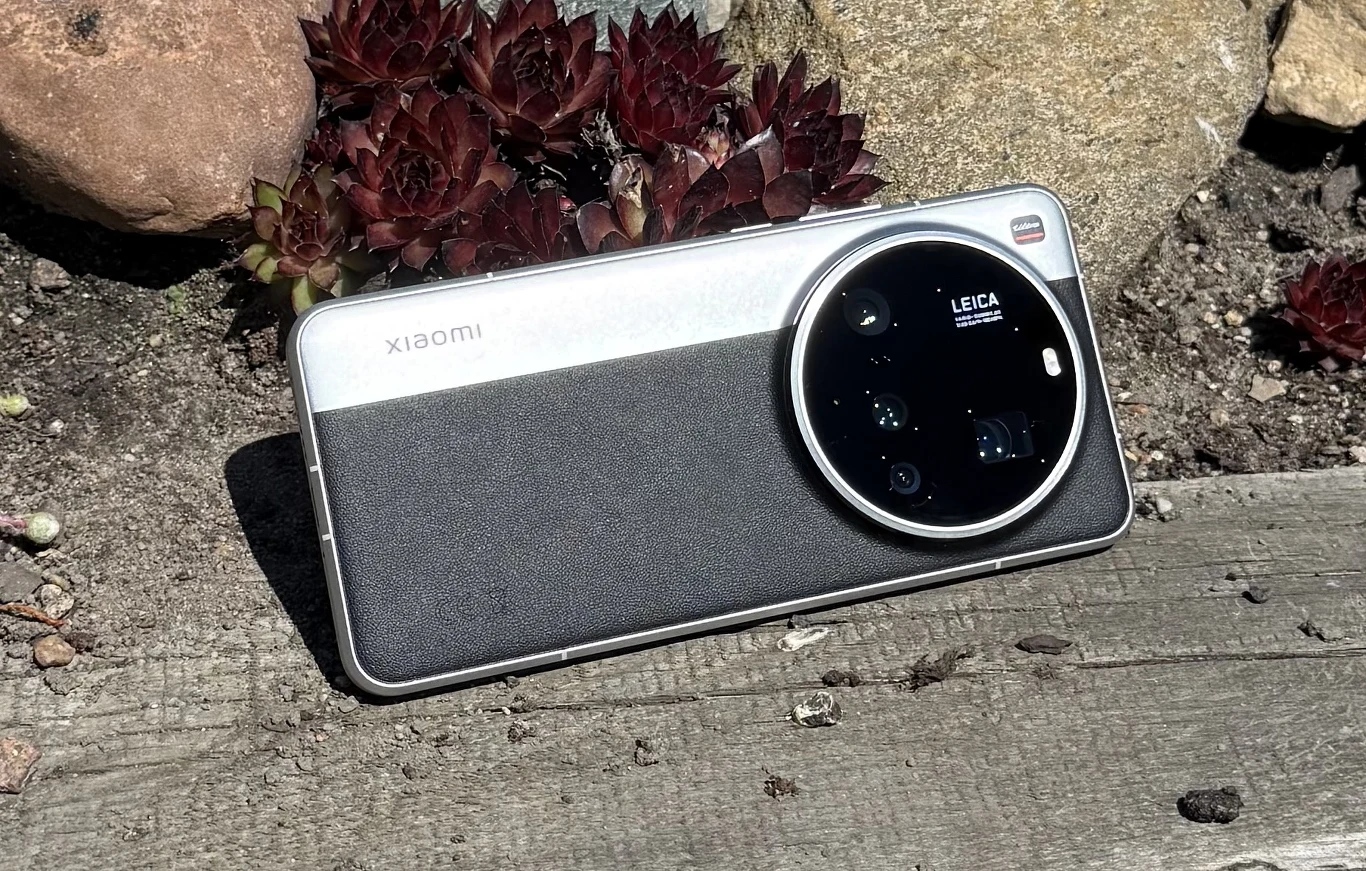 Test Xiaomi 15 Ultra. Fotoflagowiec idealny? Nowoczesny smartfon Xiaomi z dużym, okrągłym modułem aparatów oznaczonym marką Leica, leżący na drewnianej powierzchni w otoczeniu kamieni i roślin.