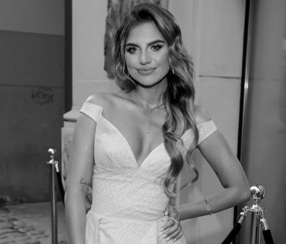 Sonia Szklanowska miała zaledwie 25 lat Kobieta w eleganckiej sukni z dekoltem, stojąca przed wejściem do budynku, z długimi falującymi włosami, uśmiechnięta, za barierkami.