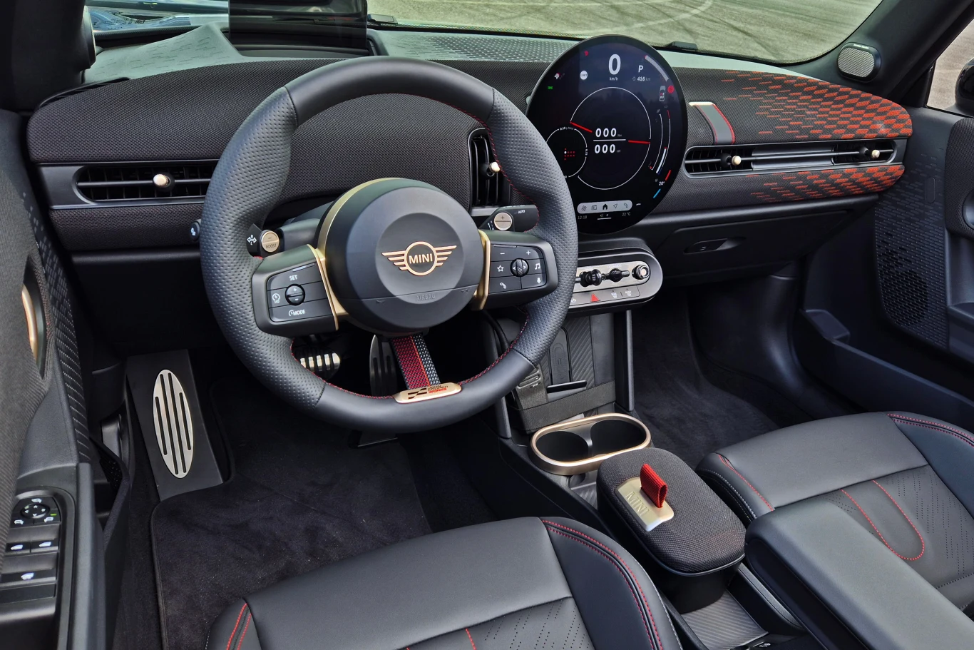 Nowoczesne wnętrze samochodu Mini z charakterystyczną kierownicą, dużym cyfrowym wyświetlaczem na desce rozdzielczej, eleganckimi fotelami ze skóry oraz designerskimi detalami na panelach przednich i konsoli środkowej.