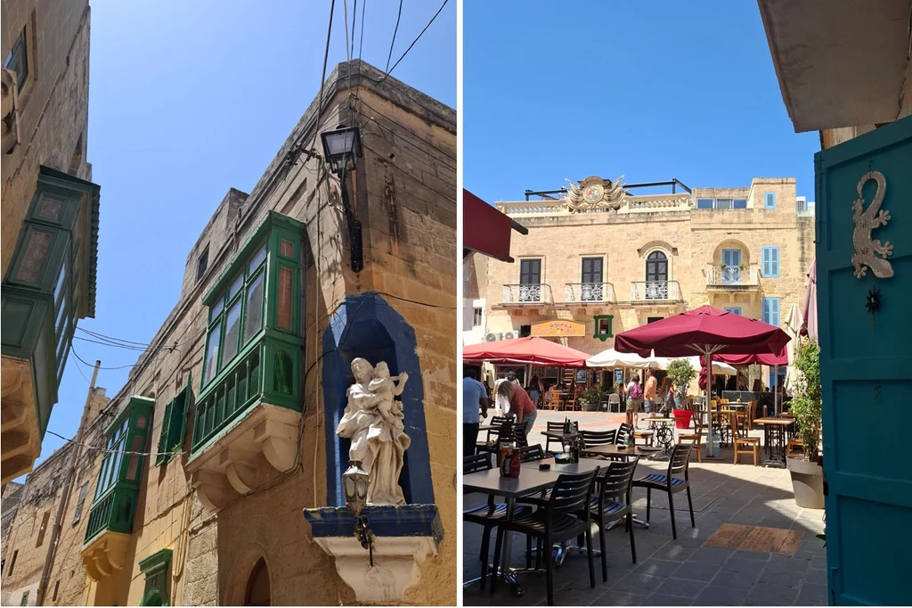 Gozo, Rabat Kamienice o piaskowej elewacji z zielonymi balkonami, rzeźba anioła na rogu budynku, jasne niebo oraz zewnętrzna restauracja z czerwonymi parasolami i rozstawionymi krzesłami na placu, gdzie przebywają ludzie.