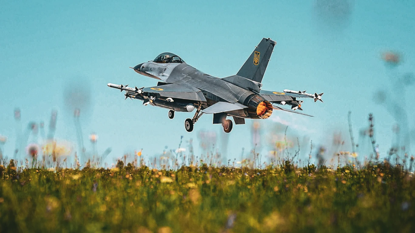 Wszystkie z holenderskich F-16 już w Ukrainie. Oświadczenie ministra obrony Myśliwiec odrzutowy startujący nad łąką, widoczny płomień z silnika, maszyna uzbrojona w pociski pod skrzydłami, jasnoniebieskie niebo w tle