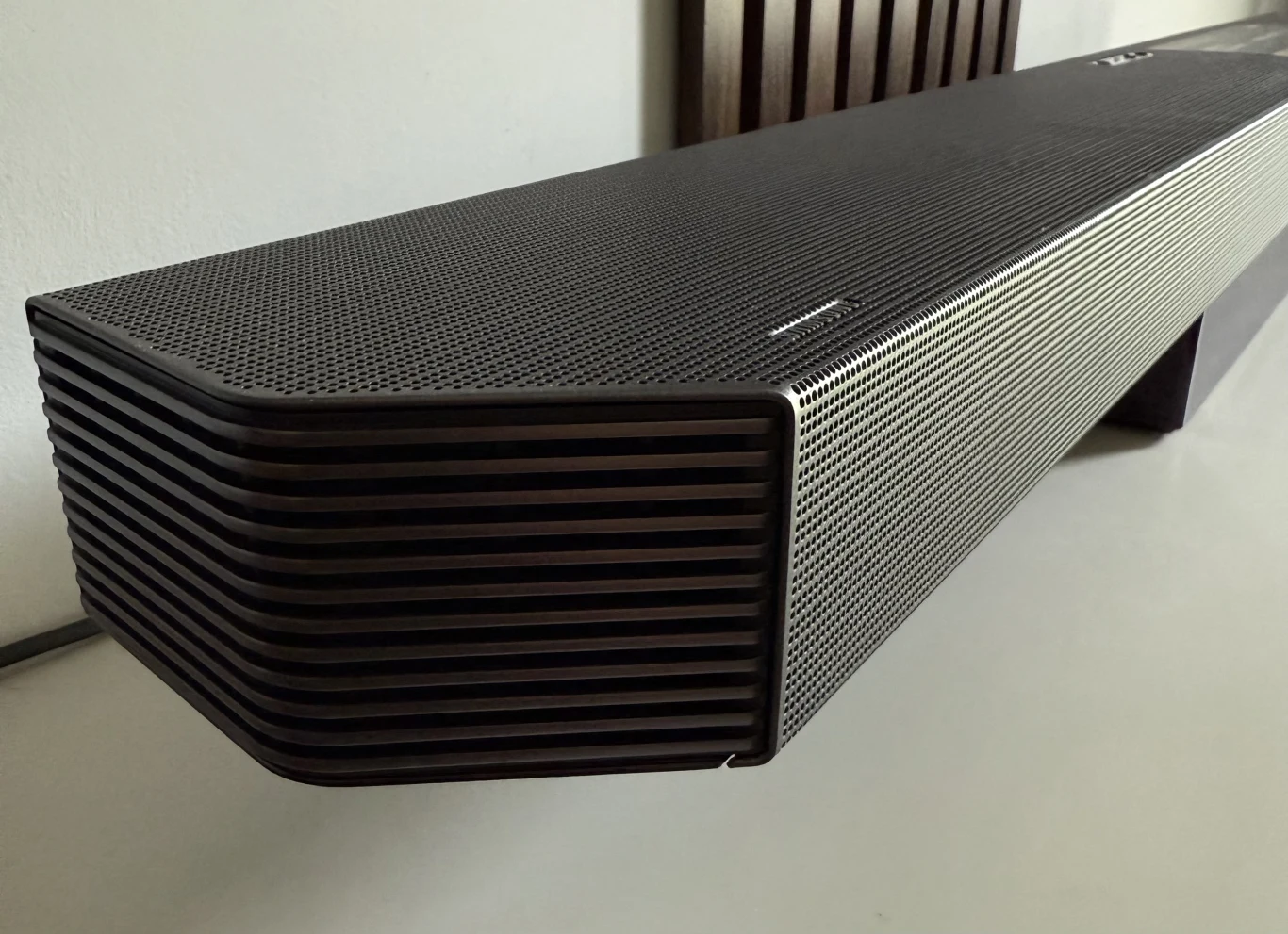 Test Samsung HW-Q930F. Soundbar o wielu możliwościach. Czarny, nowoczesny soundbar o minimalistycznym designie, ustawiony na białej powierzchni, z charakterystyczną, perforowaną obudową i wyprofilowanymi krawędziami.