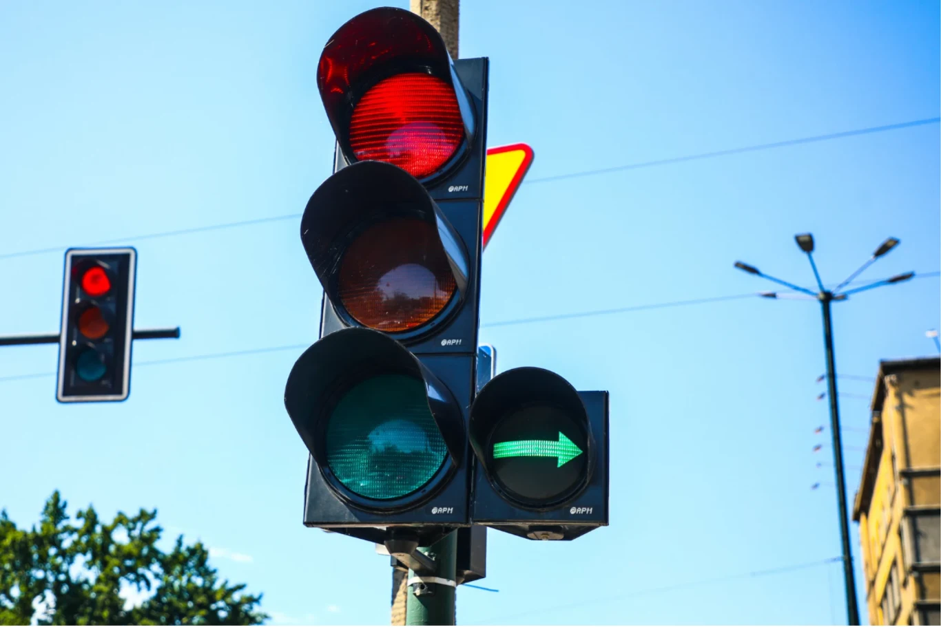 Różne kary za to samo wykroczenie? Rzecznik Praw Obywatelskich interweniuje. Sygnalizacja świetlna z włączonym czerwonym światłem i zieloną strzałką do skrętu w prawo, w tle widoczna inna sygnalizacja świetlna, fragment nieba oraz fragment budynku.