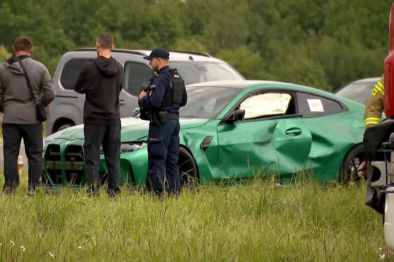 Dlaczego doszło do wypadku BMW? Fachowcy nie mają wątpliwości Policjant i kilku mężczyzn stoją obok zielonego samochodu osobowego z widocznymi uszkodzeniami po kolizji, w tle inne pojazdy oraz zieleń.