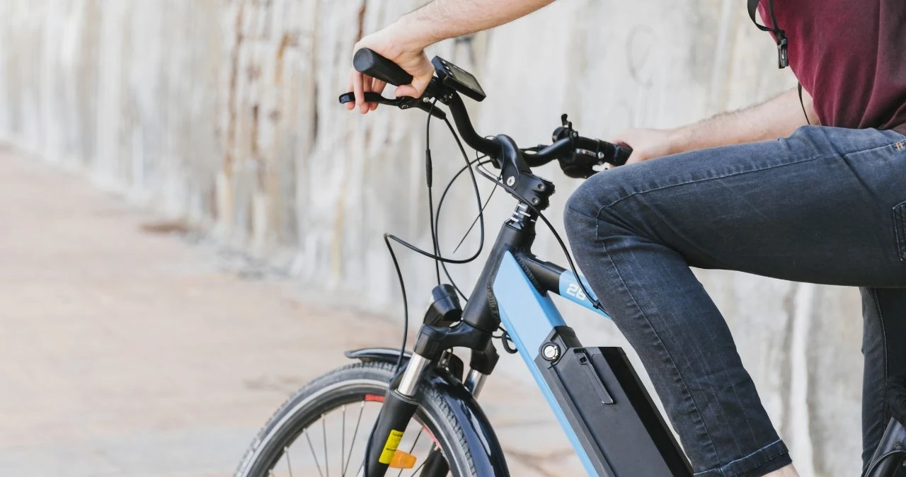 W tym mieście rowery królują. Nie brakuje tu także innych atrakcji Mężczyzna jedzie niebieskim rowerem elektrycznym wzdłuż betonowej ściany; widoczna kierownica, bateria i przednie koło.