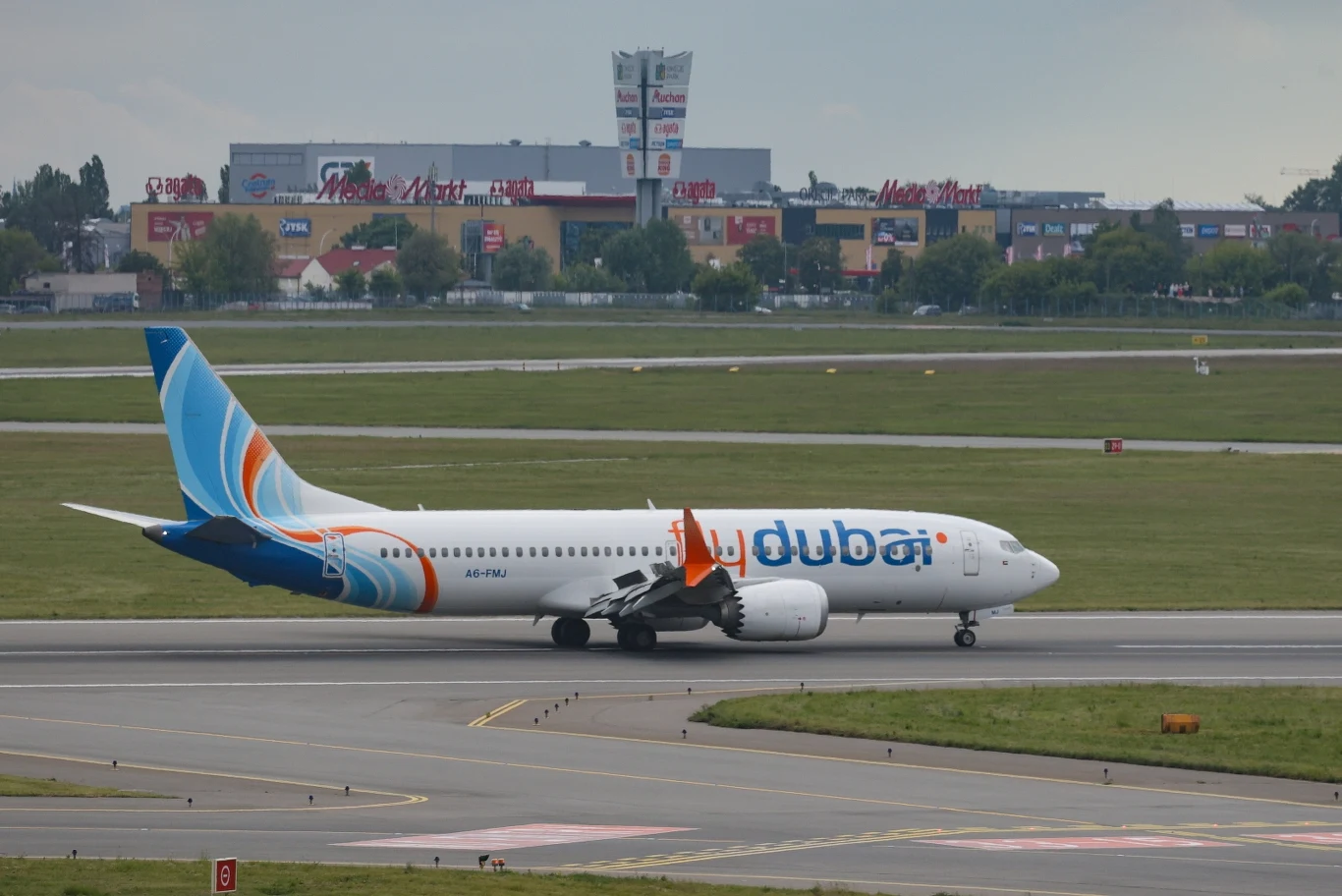 Samolot z Sebastianem M. wylądował w Warszawie Samolot pasażerski linii Flydubai znajduje się na pasie startowym lotniska, w tle widoczne są budynki komercyjne oraz tereny zielone.