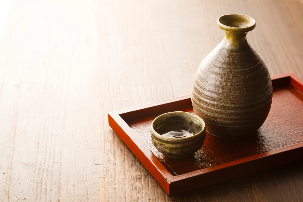 Z ryżu uruchimai produkuje się także napoje alkoholowe, np. sake Tradycyjna japońska butelka ceramiczna oraz mała miseczka z sake ustawione na czerwonej, drewnianej tacy, całość na jasnym, drewnianym stole w minimalistycznym stylu.