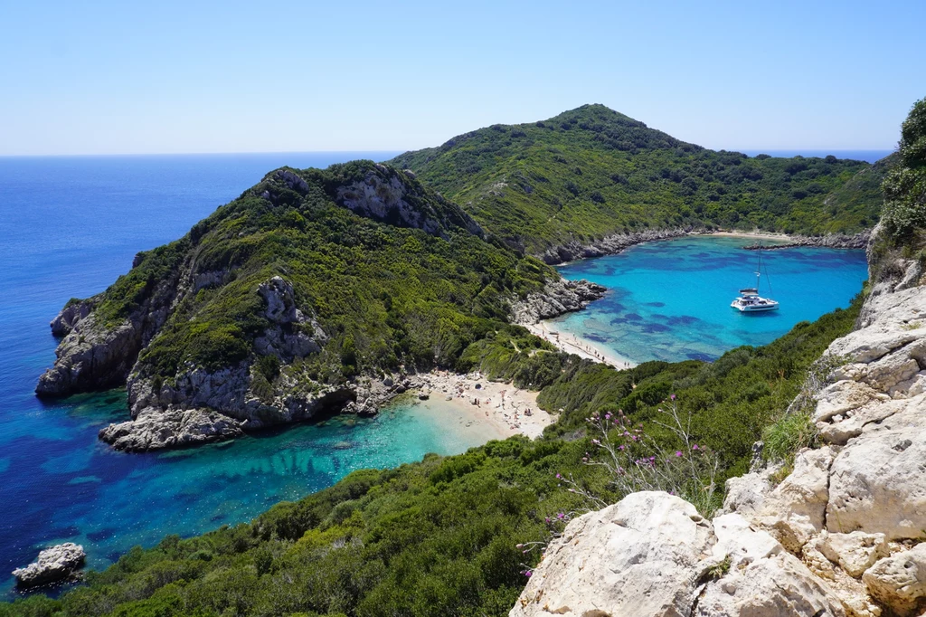 Bliźniacze plaże, czyli Porto Timoni, przypominają nieco małą Tajlandię i słynną Koh Phi Phi Malownicza zatoka otoczona zielonymi wzgórzami, z piaszczystą plażą i turkusową wodą, na której zacumowana jest biała łódź.